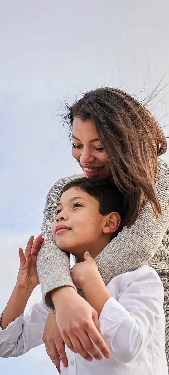 Young mother hugging her child, blue sky background with clouds. Copy space.