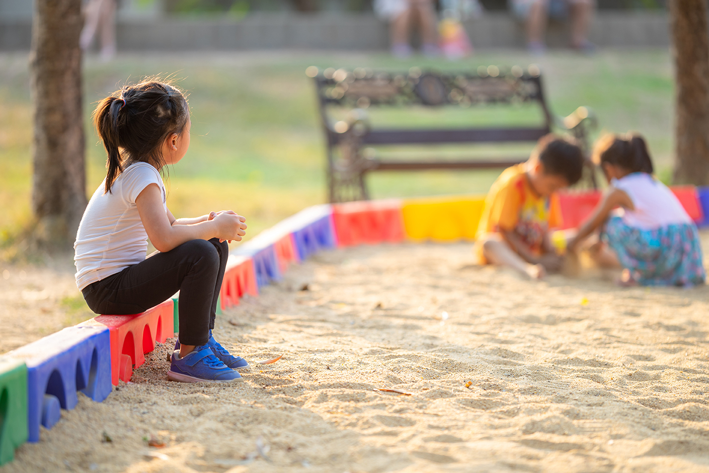 Little girl sitting lonely watching friends play at the playgrou